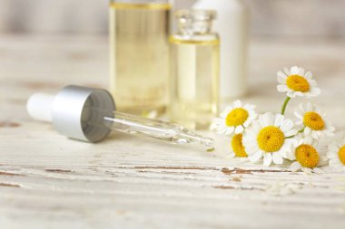 Beyaz masada uçucu yağ ve papatya çiçekleri ile Damlalık