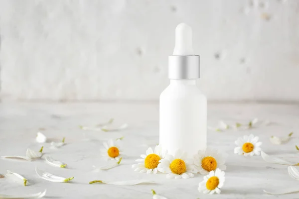 Láhev kosmetického výrobku s heřmánickými květy na světlé stolice — Stock fotografie