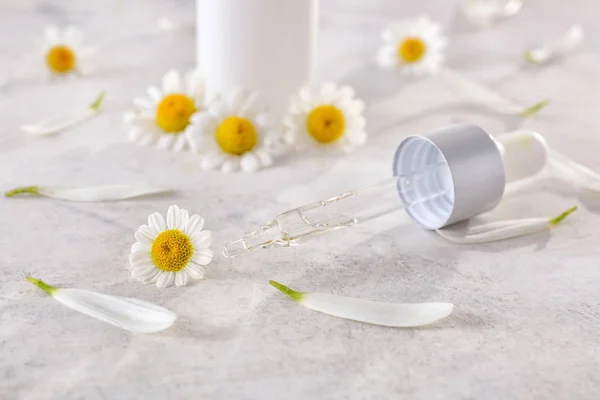 Dropper with essential oil and chamomile flowers on light table — Stock Photo, Image