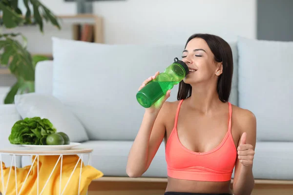 Young sporty woman drinking water from bottle at home — Stock Photo, Image