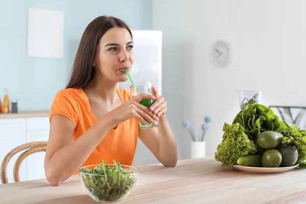 Mujer joven bebiendo jugo de verduras saludables en la cocina — Foto de Stock