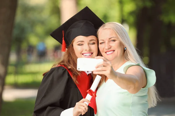 Mujer joven feliz con su madre tomando selfie en el día de la graduación — Foto de Stock