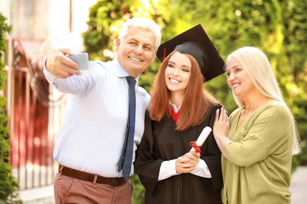 Jovem feliz com seus pais tirando selfie no dia da formatura — Fotografia de Stock