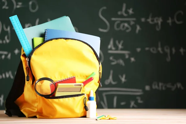 School backpack with stationery on table in classroom — Stock Photo, Image