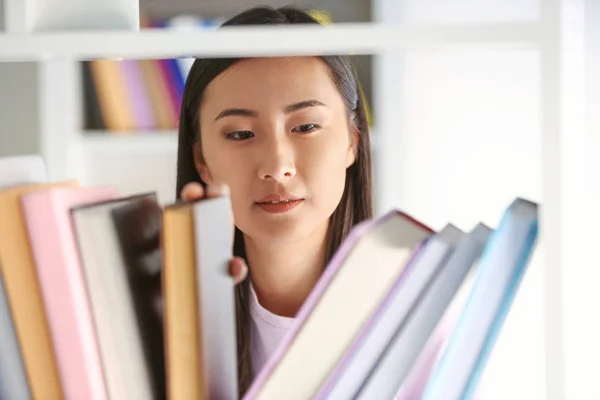 Young Asian student choosing books in library — Stock Photo, Image