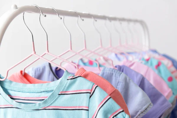 Stylish kid clothes hanging on rack against light background, closeup — Stock Photo, Image