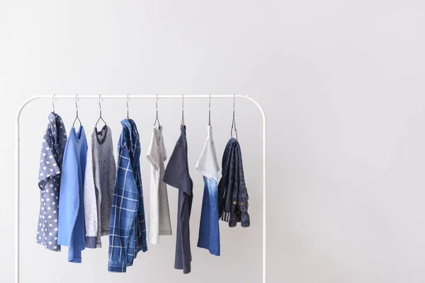 Stylish kid clothes hanging on rack against light background — Stock Photo, Image