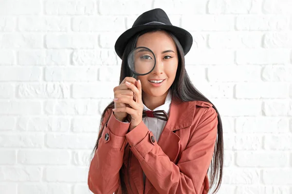 Female Asian detective with magnifying glass against white brick wall