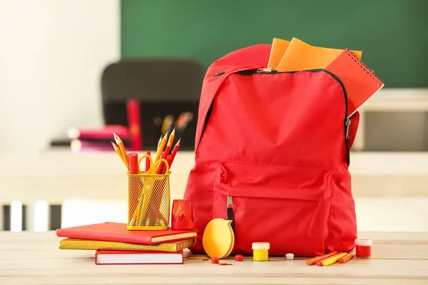 School backpack with stationery on table in classroom — Stock Photo, Image