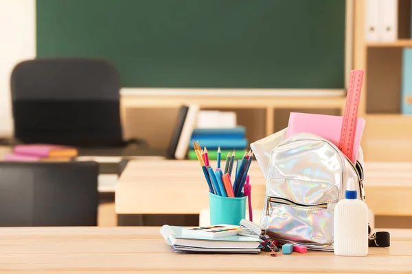 School backpack with stationery on table in classroom — Stock Photo, Image