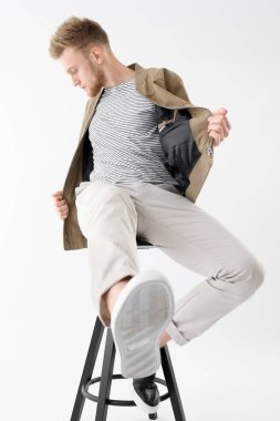 Beyaz arka plana karşı taburede oturan şık genç adam