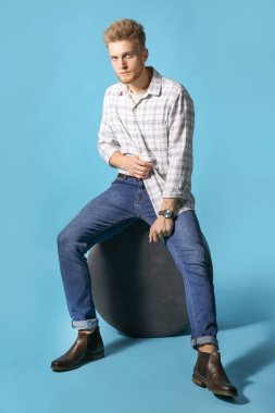 Şık genç adam renkli arka plan karşı puf üzerinde oturan