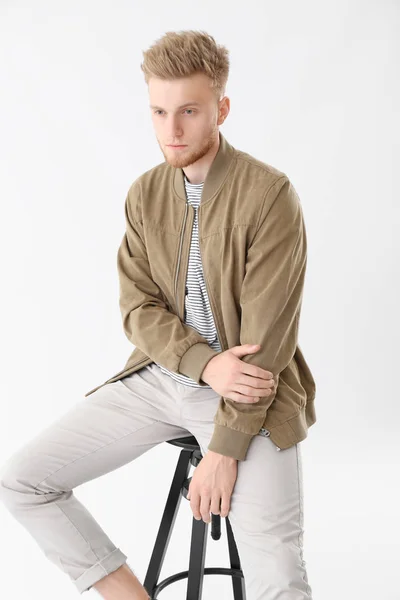 Stylish young man sitting on stool against white background — Stock Photo, Image