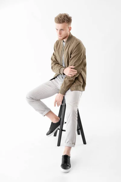 Stylischer junger Mann sitzt auf Hocker vor weißem Hintergrund — Stockfoto
