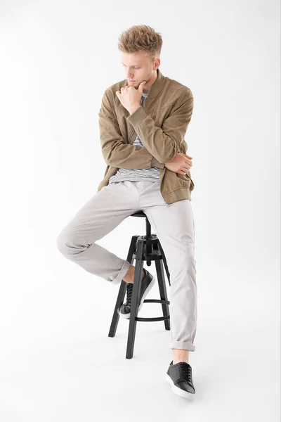 Stylischer junger Mann sitzt auf Hocker vor weißem Hintergrund — Stockfoto