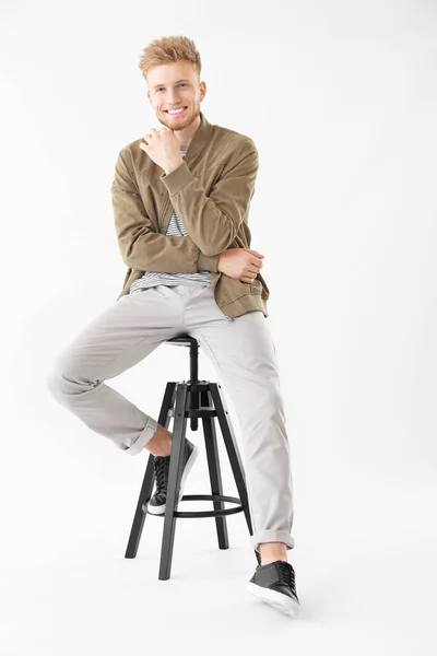 Stylish young man sitting on stool against white background — Stock Photo, Image