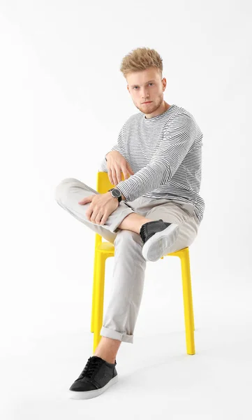 Elegante joven sentado en silla sobre fondo blanco — Foto de Stock