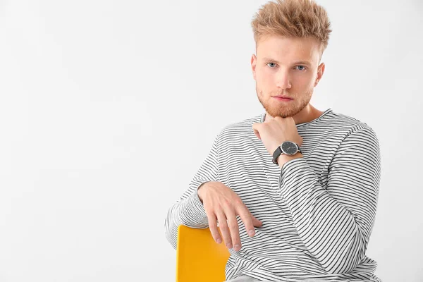 Jovem elegante sentado na cadeira contra fundo branco — Fotografia de Stock