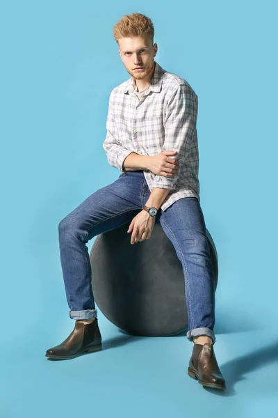 Stylish young man sitting on pouf against color background — Stock Photo, Image