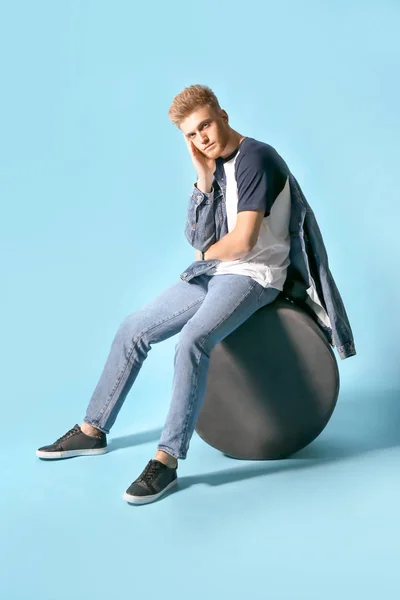 Stylish young man sitting on pouf against color background — Stock Photo, Image