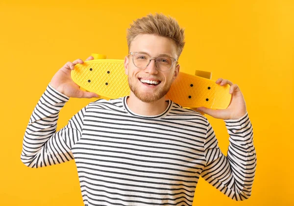 Elegante giovane uomo con skateboard su sfondo a colori — Foto Stock