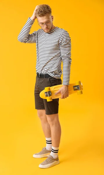 Stylish young man with skateboard on color background — Stock Photo, Image
