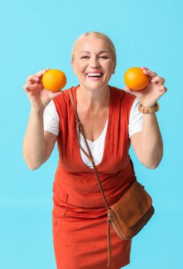 Happy mature woman with orange fruit on color background