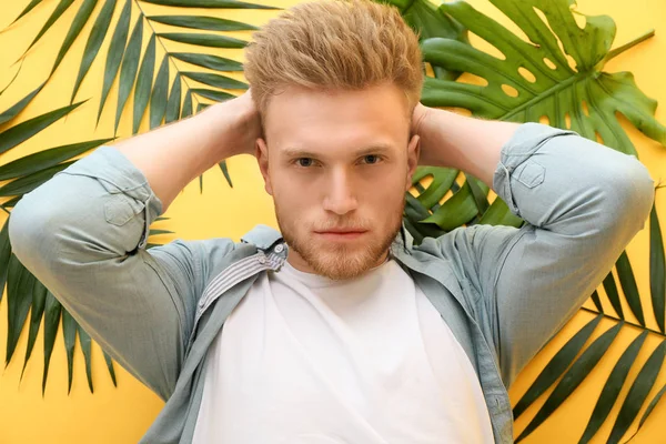 Stylish young man and tropical leaves on color background — Stock Photo, Image