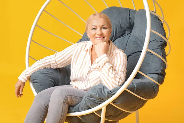 Mooie rijpe vrouw zittend in fauteuil op kleur achtergrond — Stockfoto