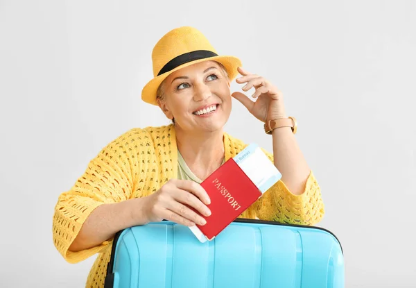 Stylish mature woman with luggage, passport and ticket on light background — Stock Photo, Image