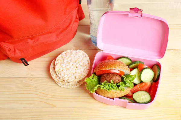 School lunch box with tasty food and backpack on table — Stock Photo, Image