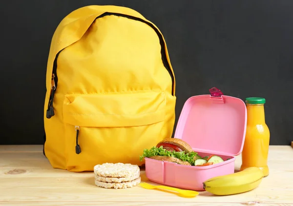 School lunch box with tasty food and backpack on table in classroom