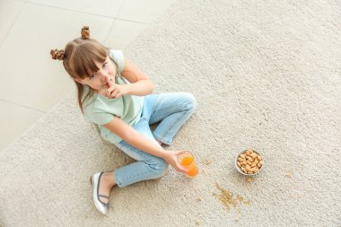 Dikkatsiz küçük kız halı üzerinde otururken fındık yeme ve meyve suyu içme