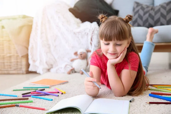 Cute little girl drawing while lying on carpet — Stock Photo, Image