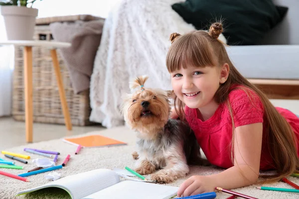 Little girl with cute dog drawing while lying on carpet