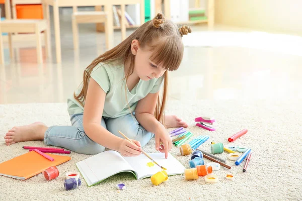 Cute little girl painting while sitting on carpet — Stock Photo, Image