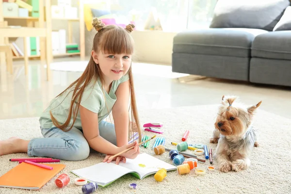 Cute little girl with dog painting while sitting on carpet — Stock Photo, Image