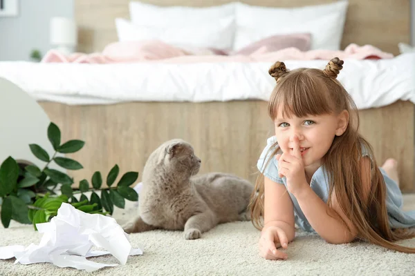 Little girl and cute cat in room with dropped houseplant and paper pieces on carpet — Stock Photo, Image