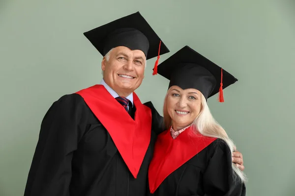 Volwassen paar in Bachelor gewaden op kleur achtergrond — Stockfoto