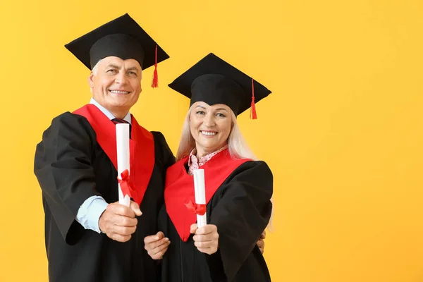 Mature couple in bachelor robes on color background — Stock Photo, Image