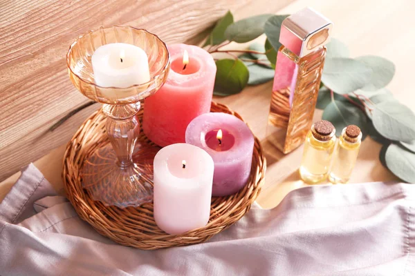 Hermosas velas encendidas con aceite esencial y botella de perfume en la mesa de madera —  Fotos de Stock