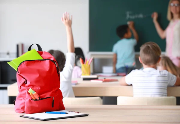 Rugzak met briefpapier op tafel in de klas — Stockfoto