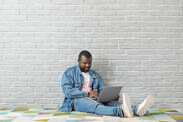 African-American blogger with laptop sitting near brick wall — Stock Photo, Image