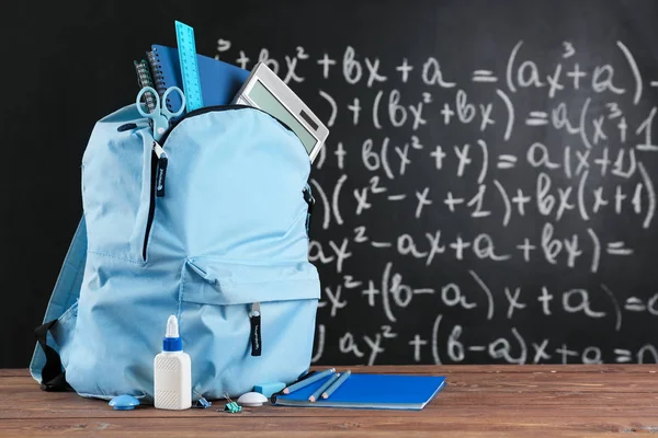 School backpack with stationery on table in classroom — Stock Photo, Image