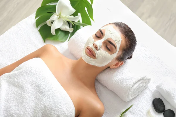Bella giovane donna con maschera facciale rilassante nel salone spa — Foto Stock