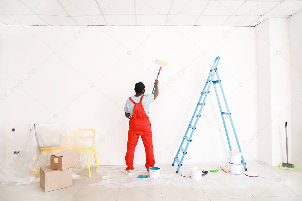 African-American decorator painting light wall in room