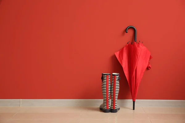 Stylish umbrella with gumboots near color wall — Stock Photo, Image