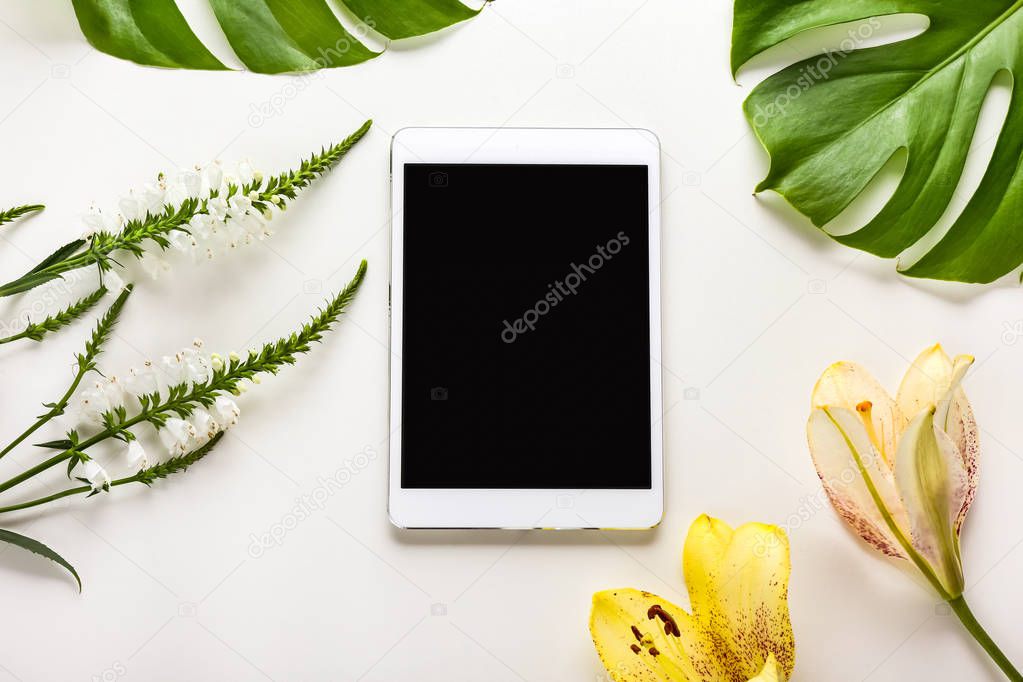 Tablet computer, flowers and tropical leaves on white background