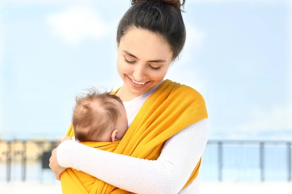 Young mother with her baby in sling walking outdoors — Stock Photo, Image