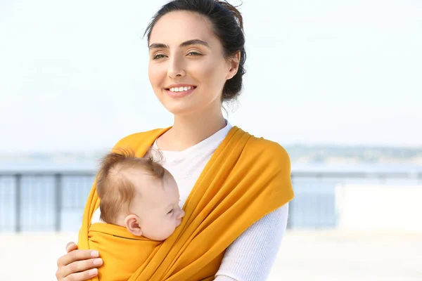 Young mother with her baby in sling walking outdoors — Stock Photo, Image